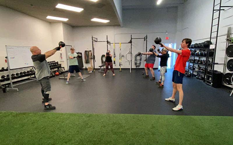 Tucson Strength Services - Group Fitness Training. Instructor demonstrates kettlebell swing to group fitness class.